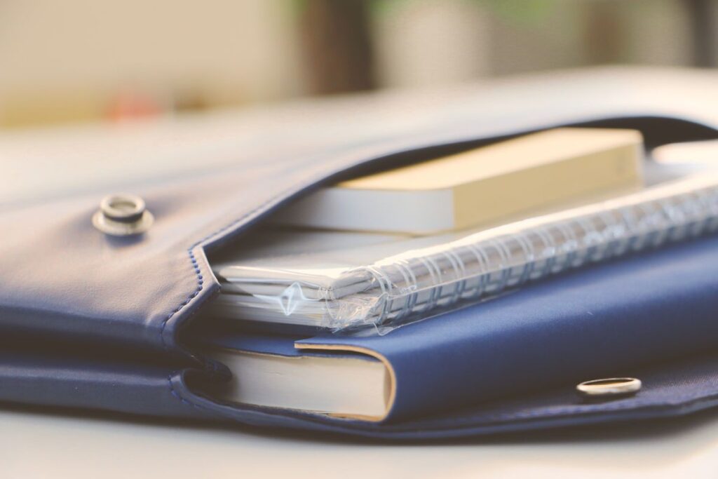 A blue leather portfolio holds a spiral notebook and a closed book on a desk.