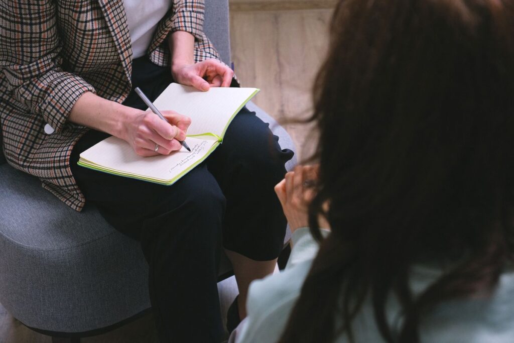 Therapist writes in a notebook while a client sits nearby during a counseling session