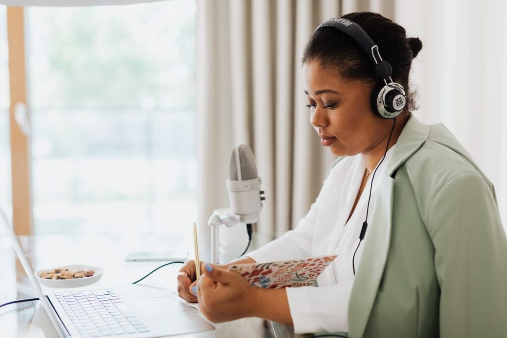 Woman wearing headphones writes in a notebook beside a microphone